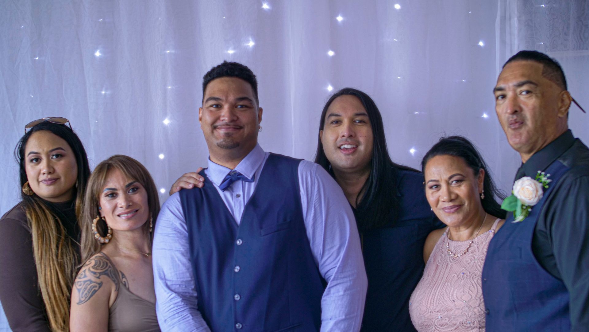 Group of people dressed in formal attire standing together in front of a backdrop with string lights.