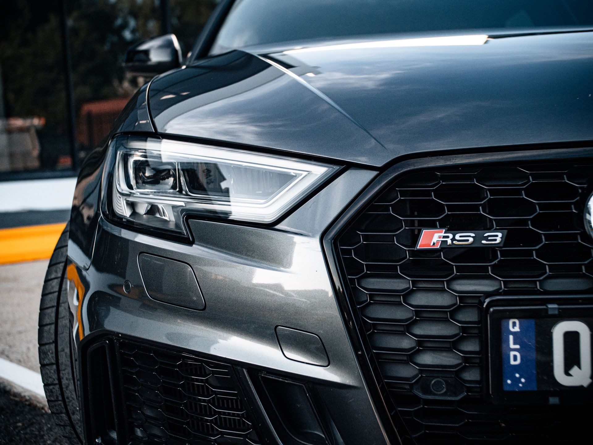 Close-up of a sleek, dark-colored Audi RS3 front with headlights and grille visible.