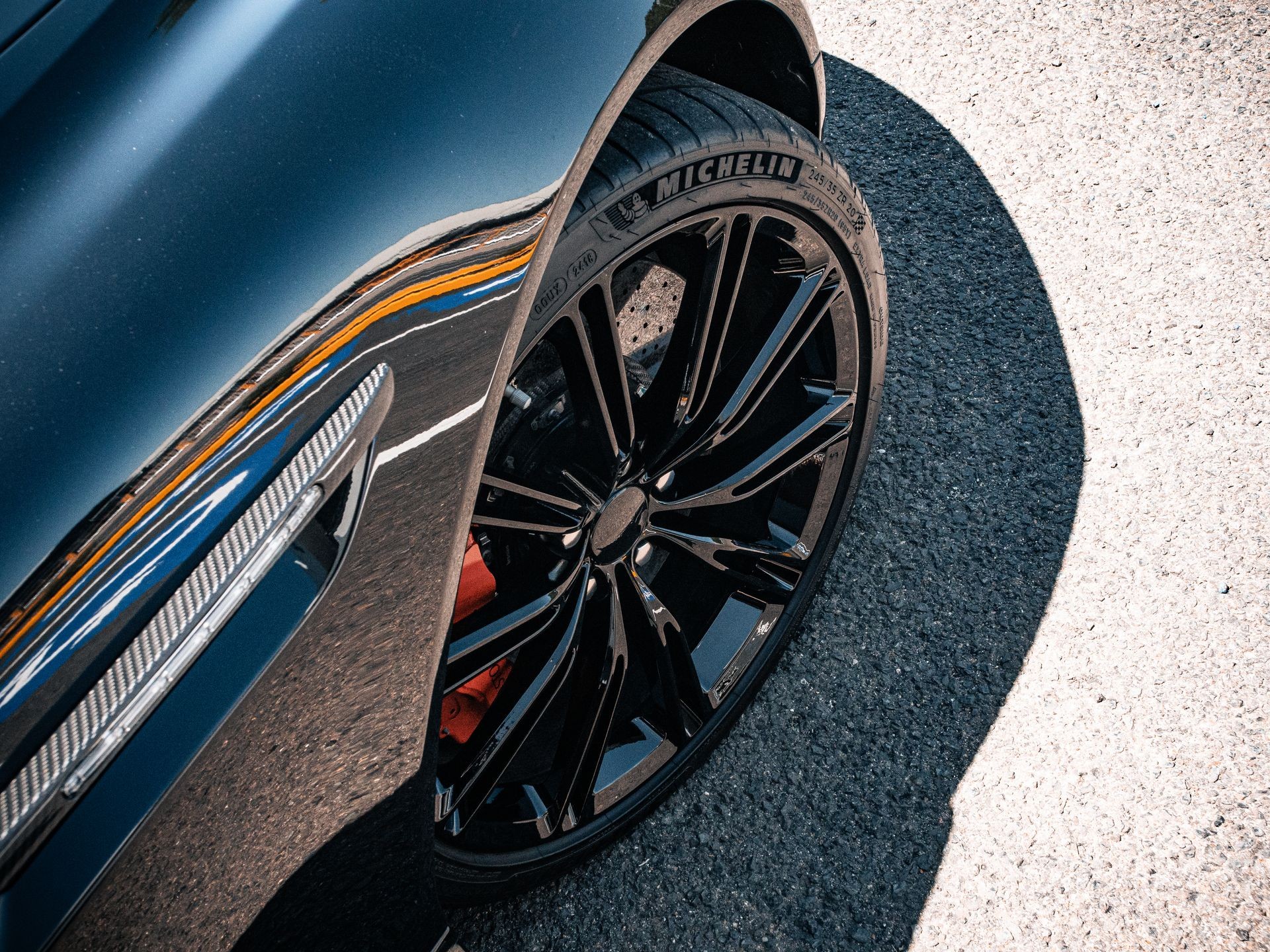 Close-up view of a black car's shiny wheel with a Michelin tire on an asphalt road.